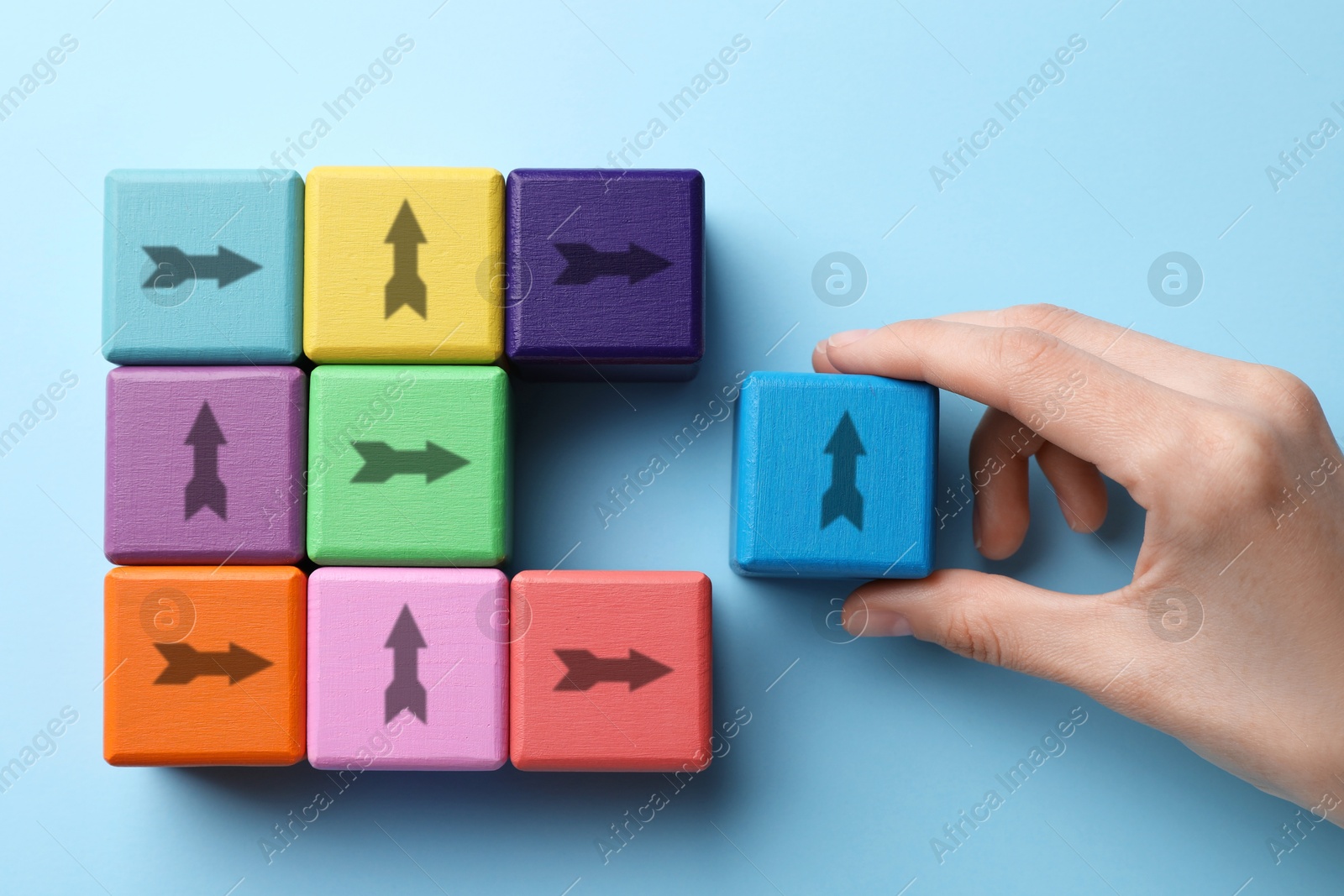 Image of Woman holding cube with arrow on light blue background, top view