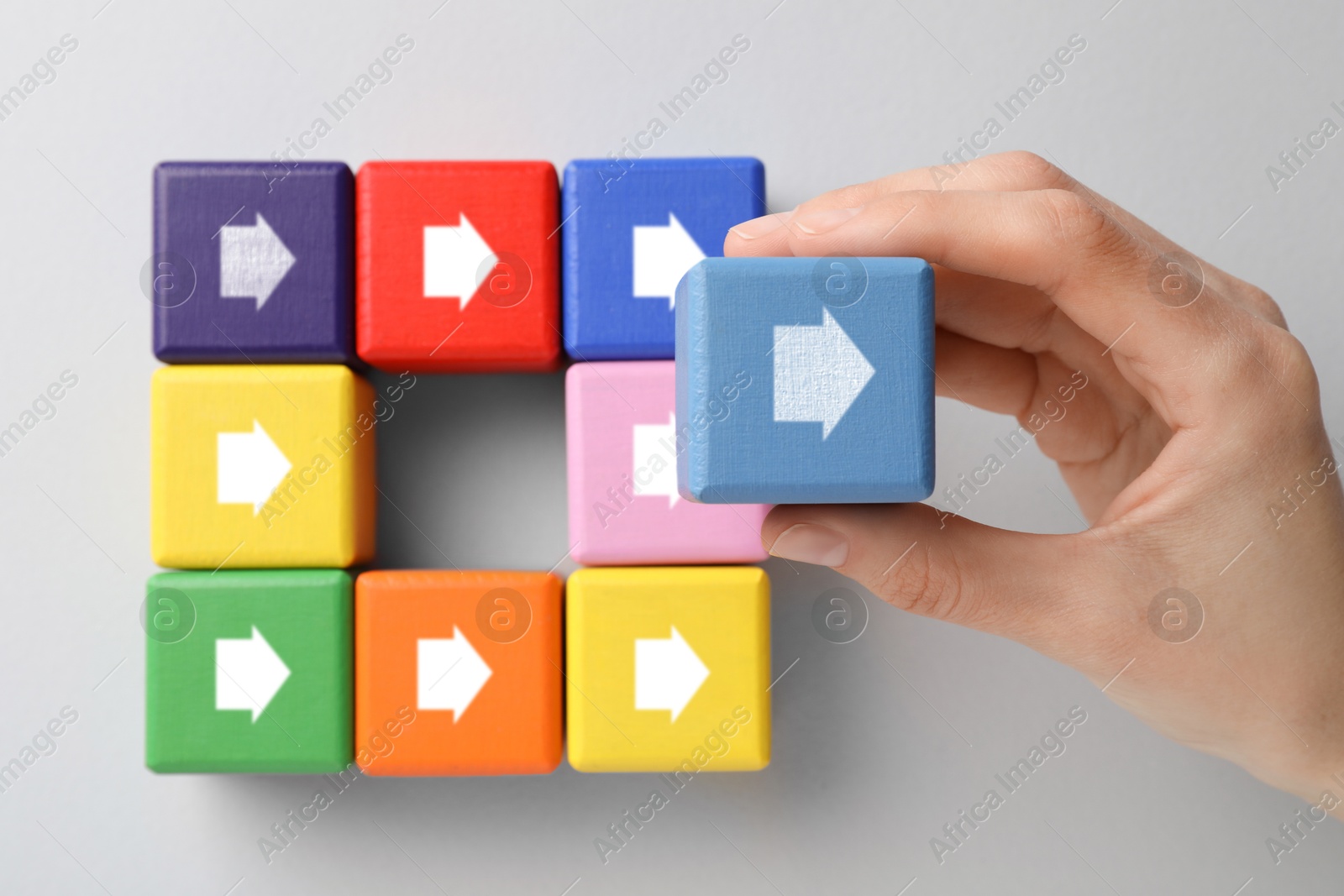 Image of Woman holding cube with arrow on light grey background, top view