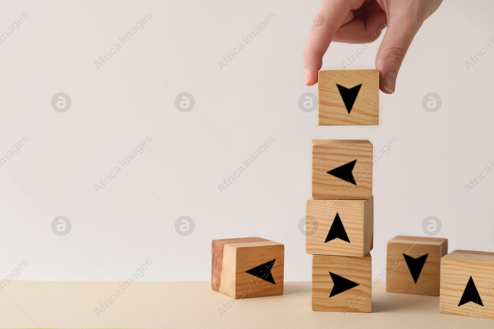 Image of Woman stacking cubes with black arrows on wooden table, closeup. Space for text