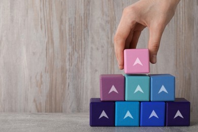 Image of Woman stacking cubes with arrows on wooden table, closeup. Space for text