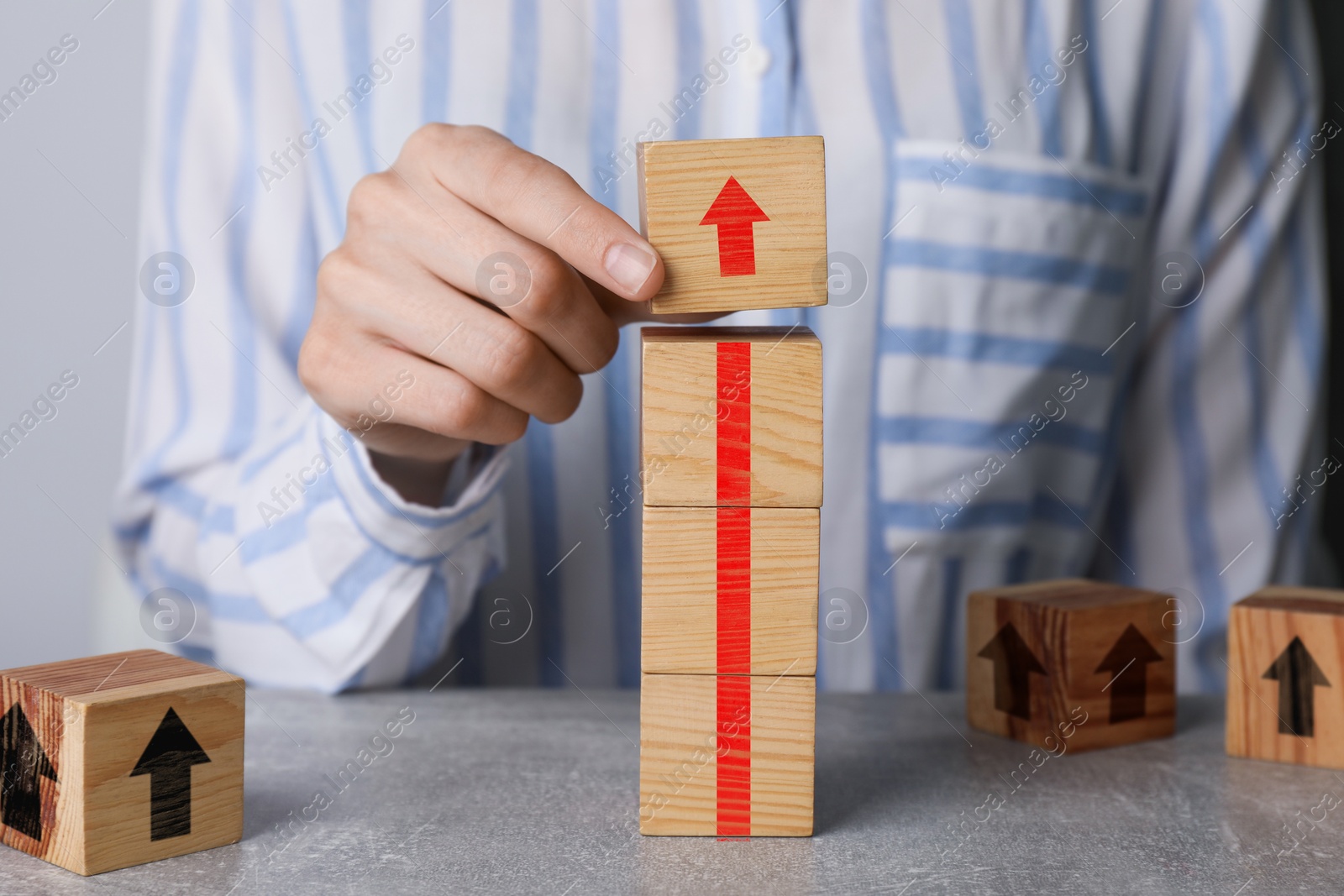 Image of Woman making red arrow of wooden cubes on grey table, closeup