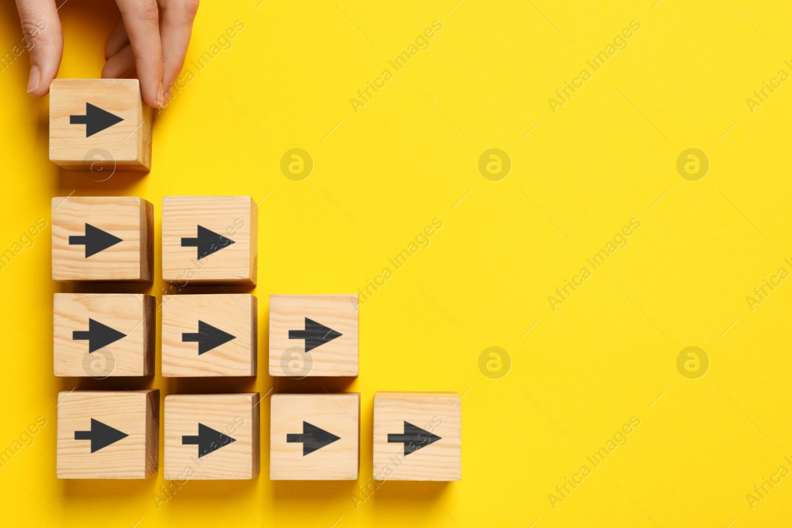 Image of Woman holding cube with black arrow on yellow background, top view. Space for text