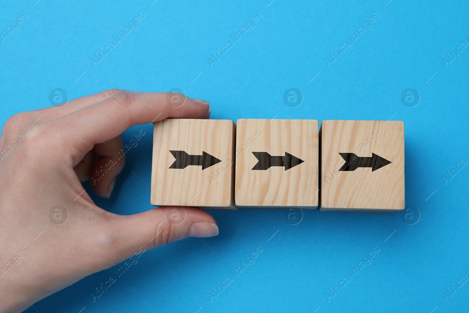 Image of Woman holding wooden cube with arrow on light blue background, closeup