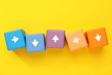 Image of Colorful cubes with white arrows on yellow background, top view