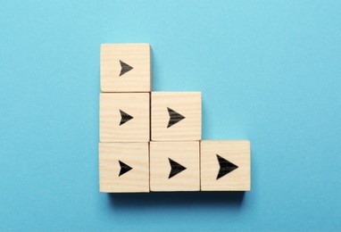 Image of Wooden cubes with black arrows on light blue background, top view. Pointers from smallest to bigger