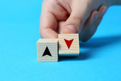 Image of Woman holding wooden cube with red arrow on light blue background, closeup