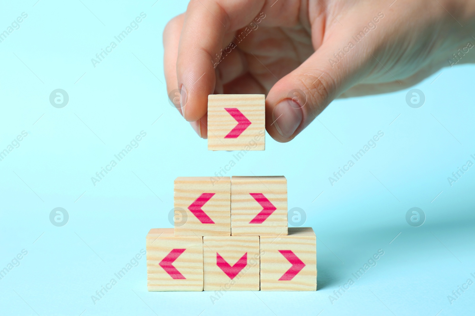 Image of Woman stacking wooden cubes with pink arrows on light blue background, closeup