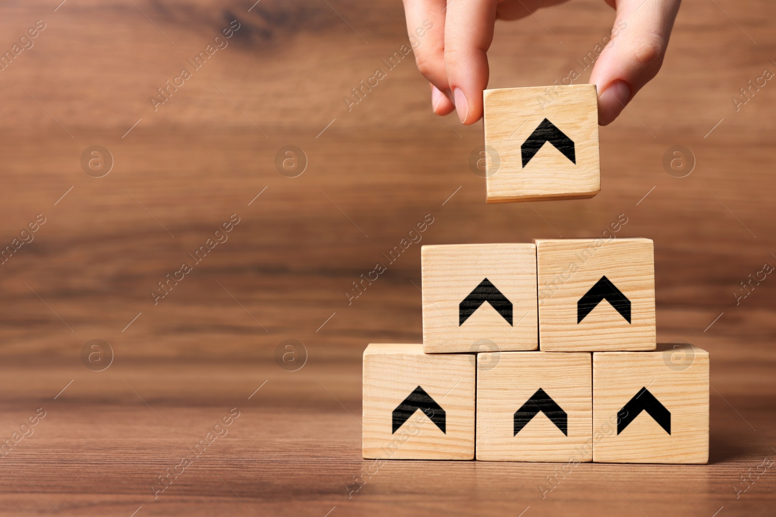 Image of Woman stacking wooden cubes with black arrows on wooden background, closeup. Space for text