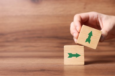 Image of Woman holding cube with green arrow on wooden table, closeup. Space for text