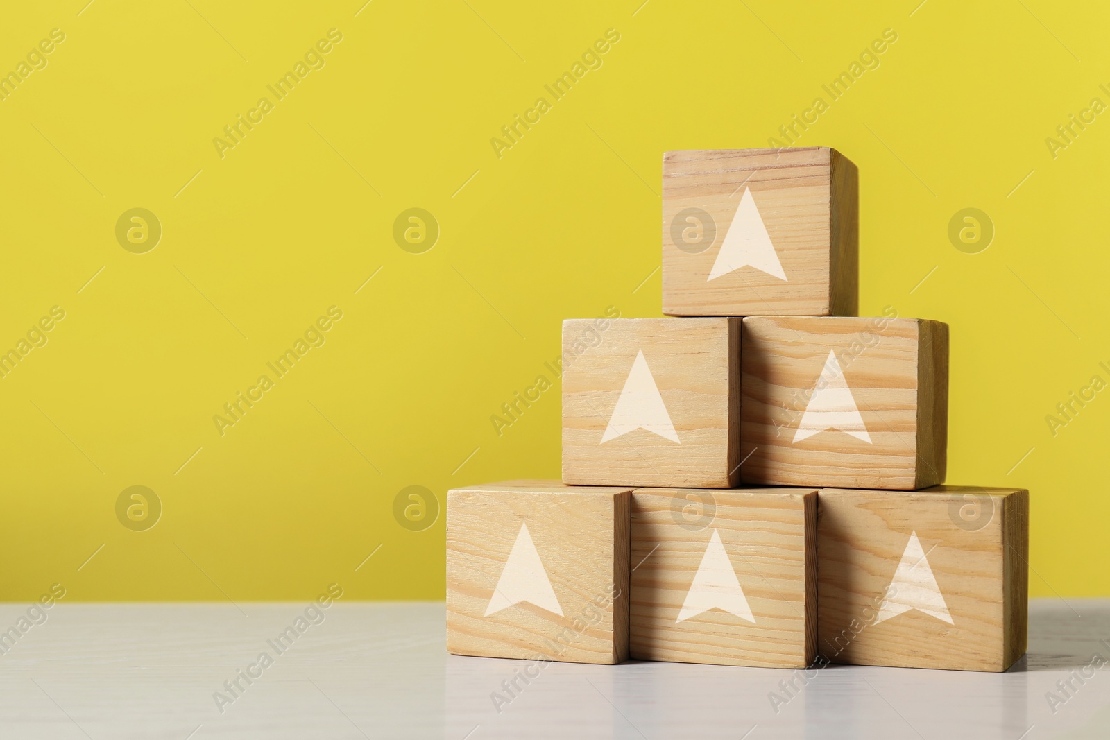 Image of Wooden cubes with arrows on table against yellow background, space for text