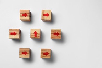 Image of Wooden cubes with red arrows pointing in different directions on white background, top view. Space for text