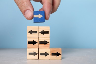 Image of Man putting cube with arrow on top of pyramid against light blue background, closeup