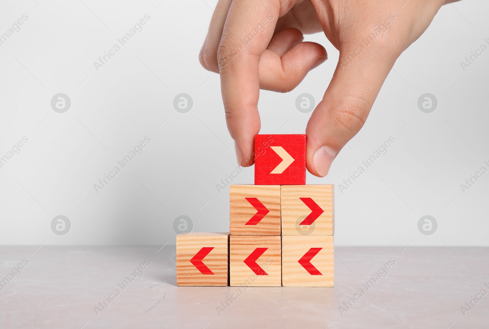 Image of Woman putting red cube with arrow on top of pyramid against light background, closeup