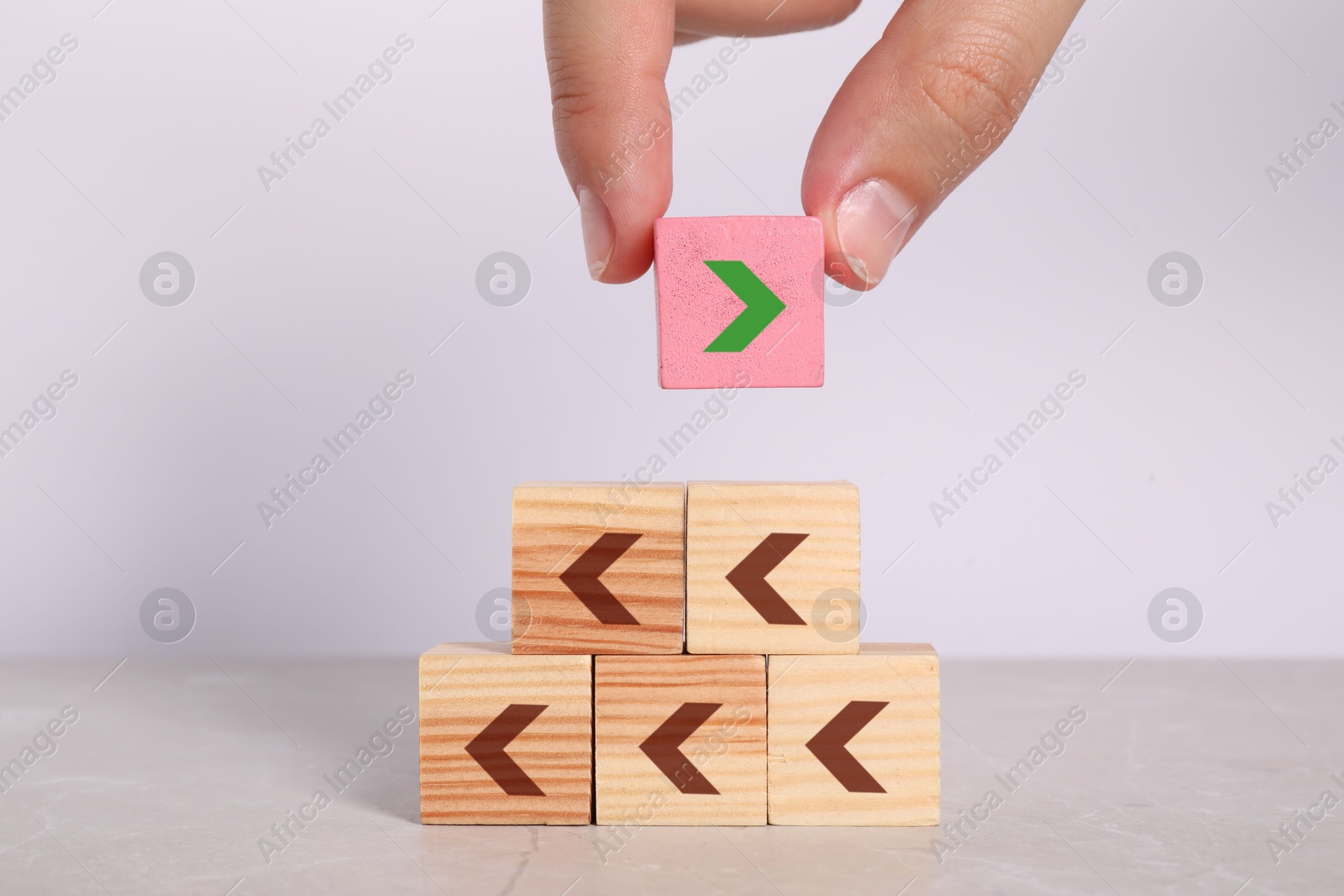 Image of Woman putting pink cube with arrow on top of pyramid against light background, closeup