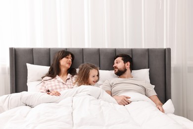 Photo of Playful daughter with her overwhelmed parents in bed at home