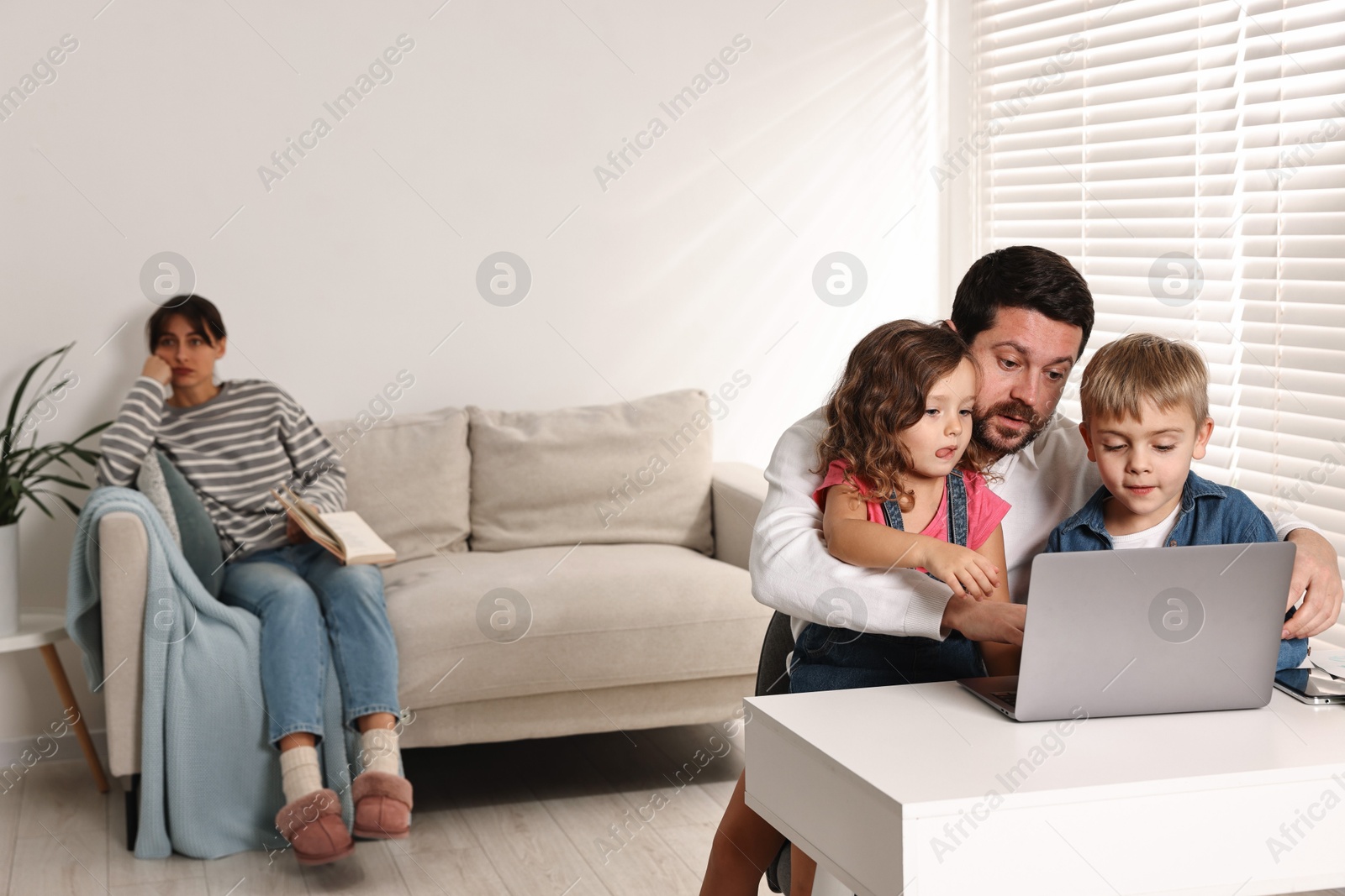 Photo of Father with children using laptop while their overwhelmed mother on sofa at home