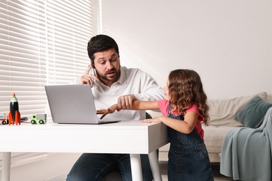 Photo of Naughty daughter disturbing her overwhelmed father while he talking on smartphone at table indoors