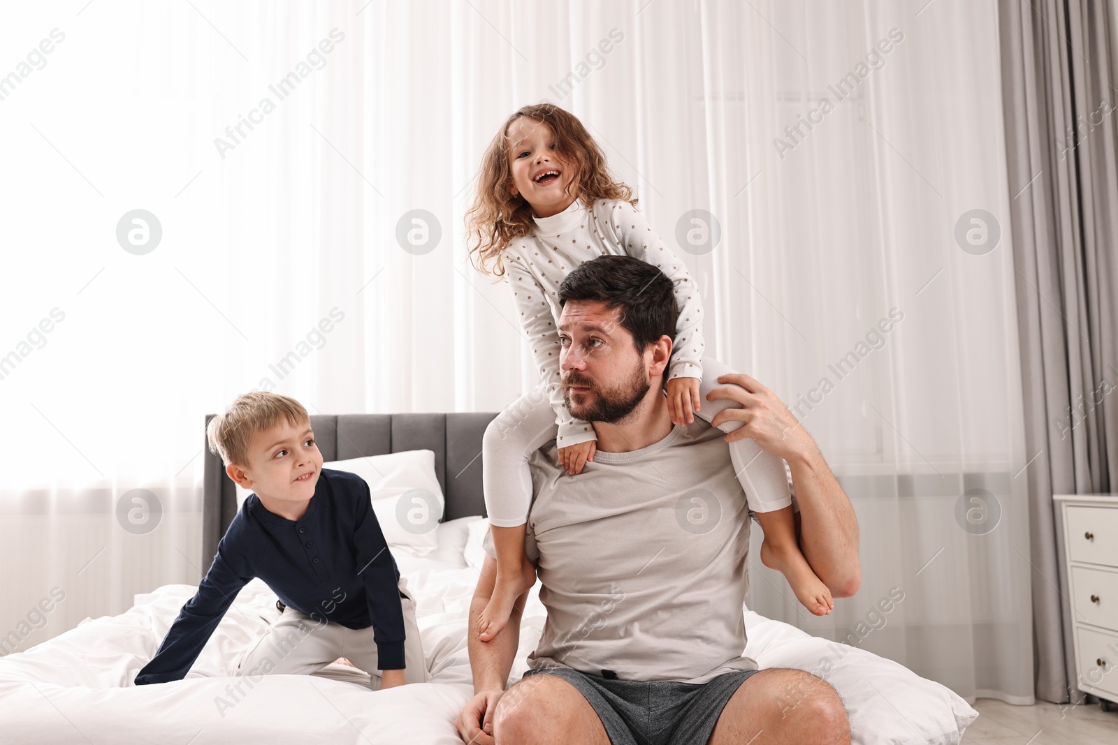 Photo of Overwhelmed father and his playful children on bed at home