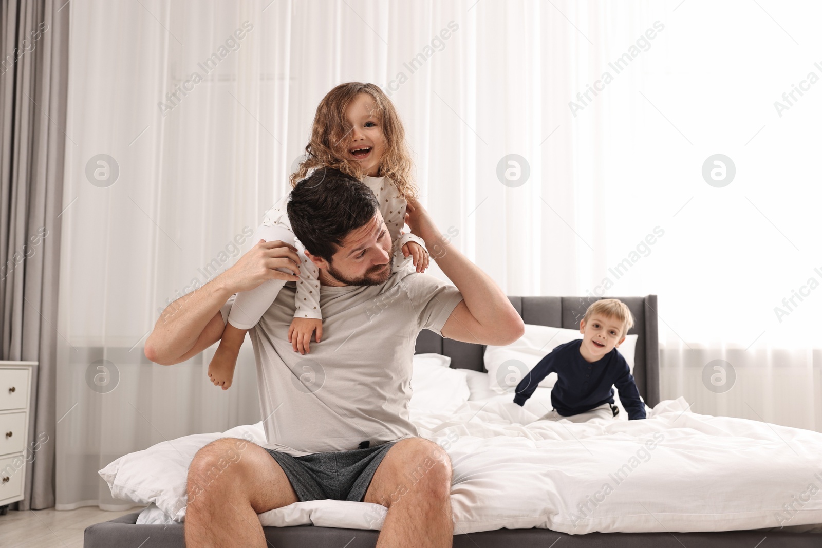 Photo of Overwhelmed father and his playful children on bed at home