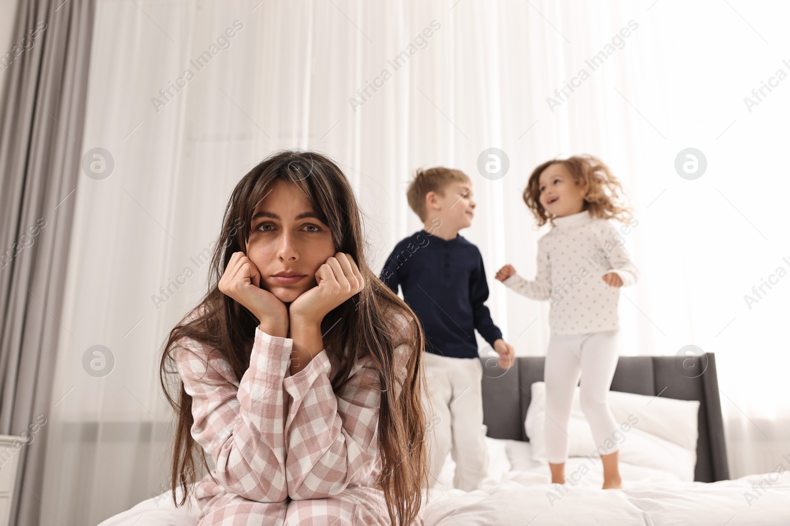 Photo of Overwhelmed mother and her playful children on bed at home, selective focus