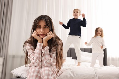 Photo of Overwhelmed mother and her playful children on bed at home, selective focus