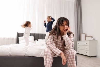 Photo of Overwhelmed mother and her playful children on bed at home, selective focus