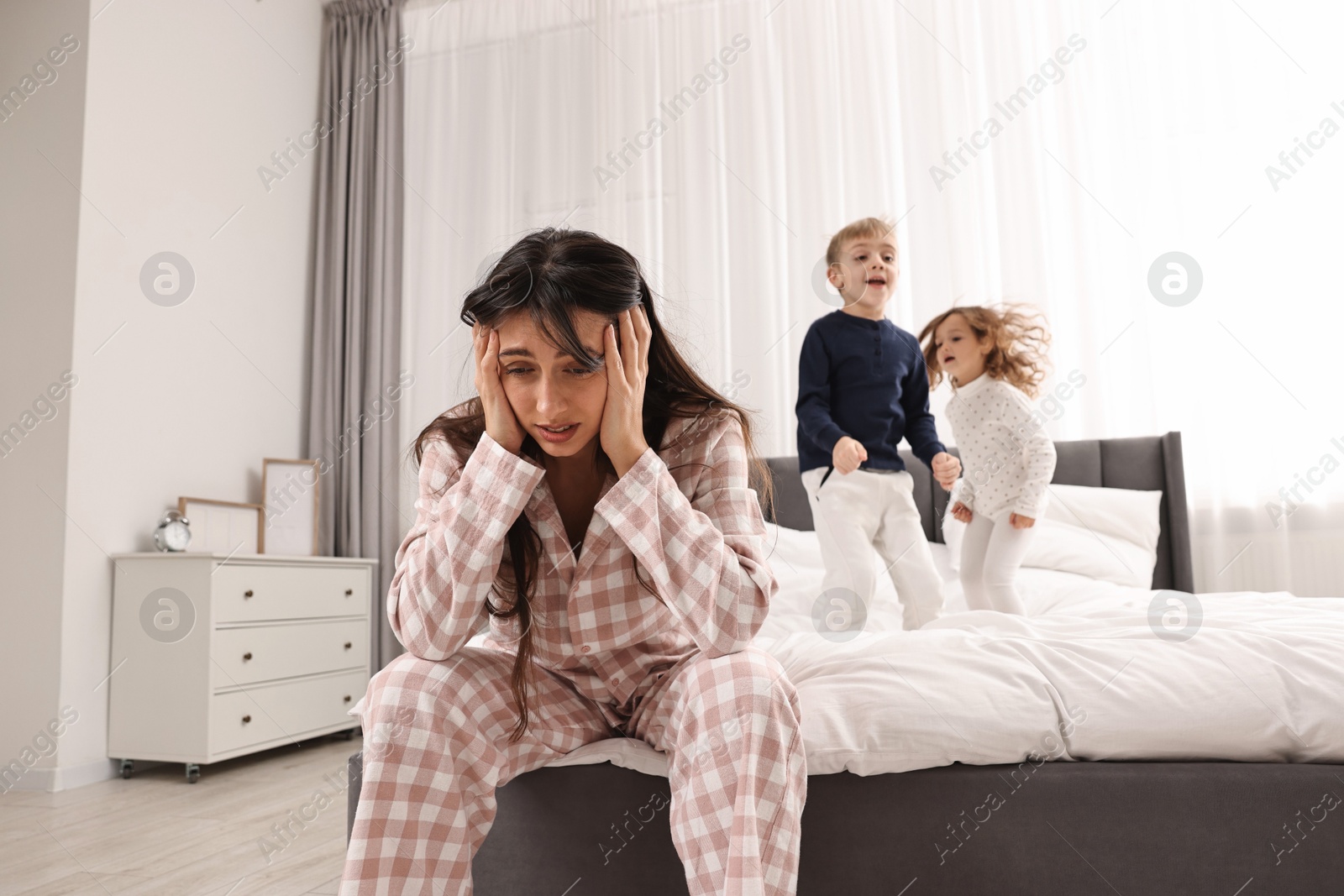 Photo of Overwhelmed mother and her playful children on bed at home