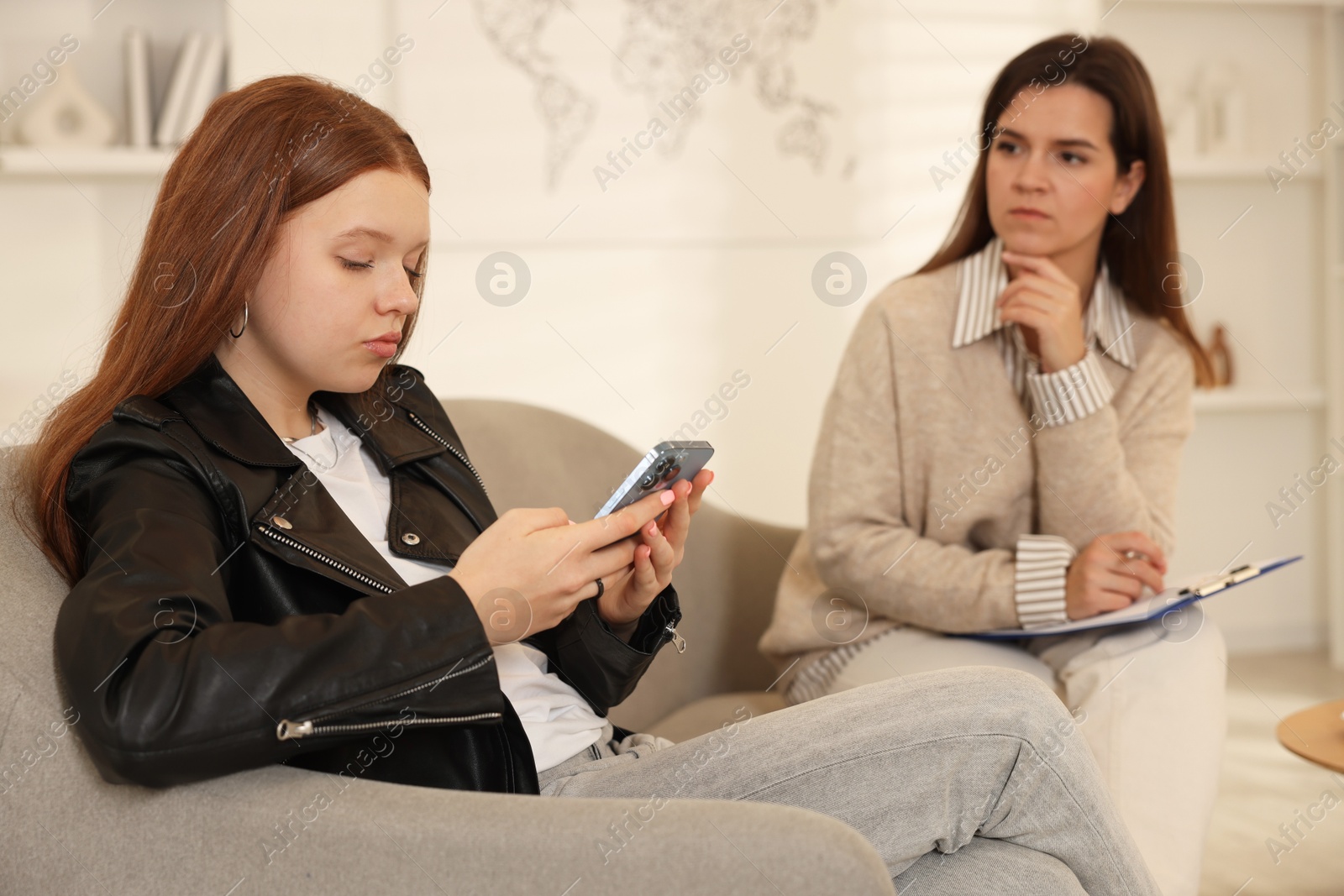 Photo of Rebellious teenage girl using smartphone instead of consultation with psychologist in office, selective focus