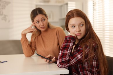 Photo of Annoyed teenage girl with smartphone and her mother at psychologist's office, selective focus