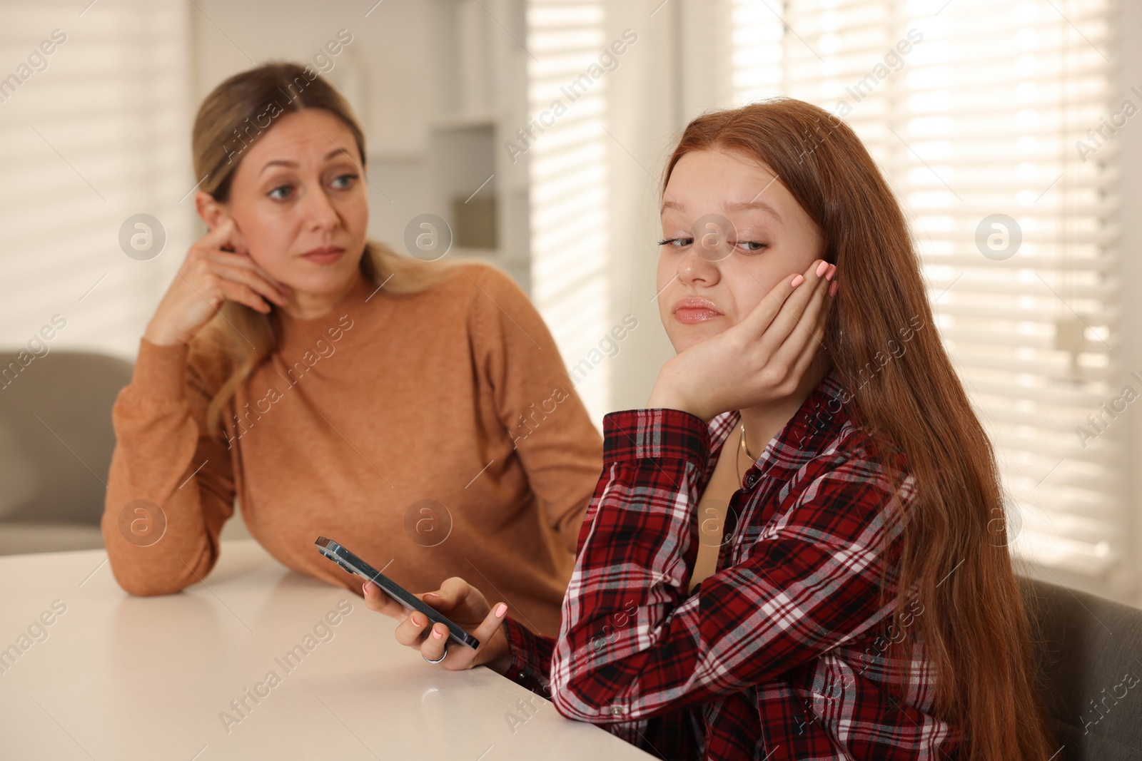 Photo of Annoyed teenage girl with smartphone and her mother at psychologist's office, selective focus