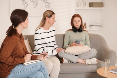 Photo of Teenage girl using smartphone while having consultation with her mom and psychologist indoors