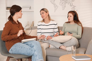 Photo of Teenage girl listening to music instead of working with psychologist in office. Mother and daughter difficult relationship