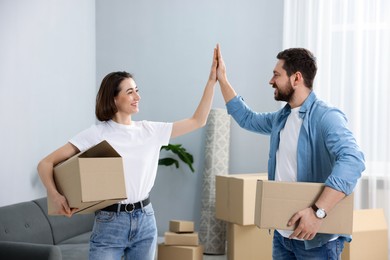 Photo of Moving day. Happy couple with cardboard boxes giving each other high five in their new home