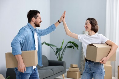 Photo of Moving day. Happy couple with cardboard boxes giving each other high five in their new home