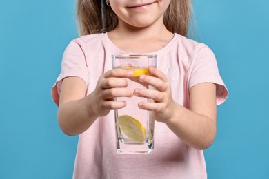 Photo of Girl with glass of lemonade on light blue background, closeup. Refreshing drink