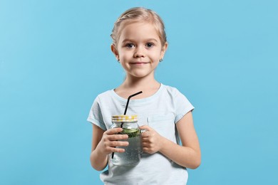 Photo of Girl with mason jar of cucumber water on light blue background. Refreshing drink