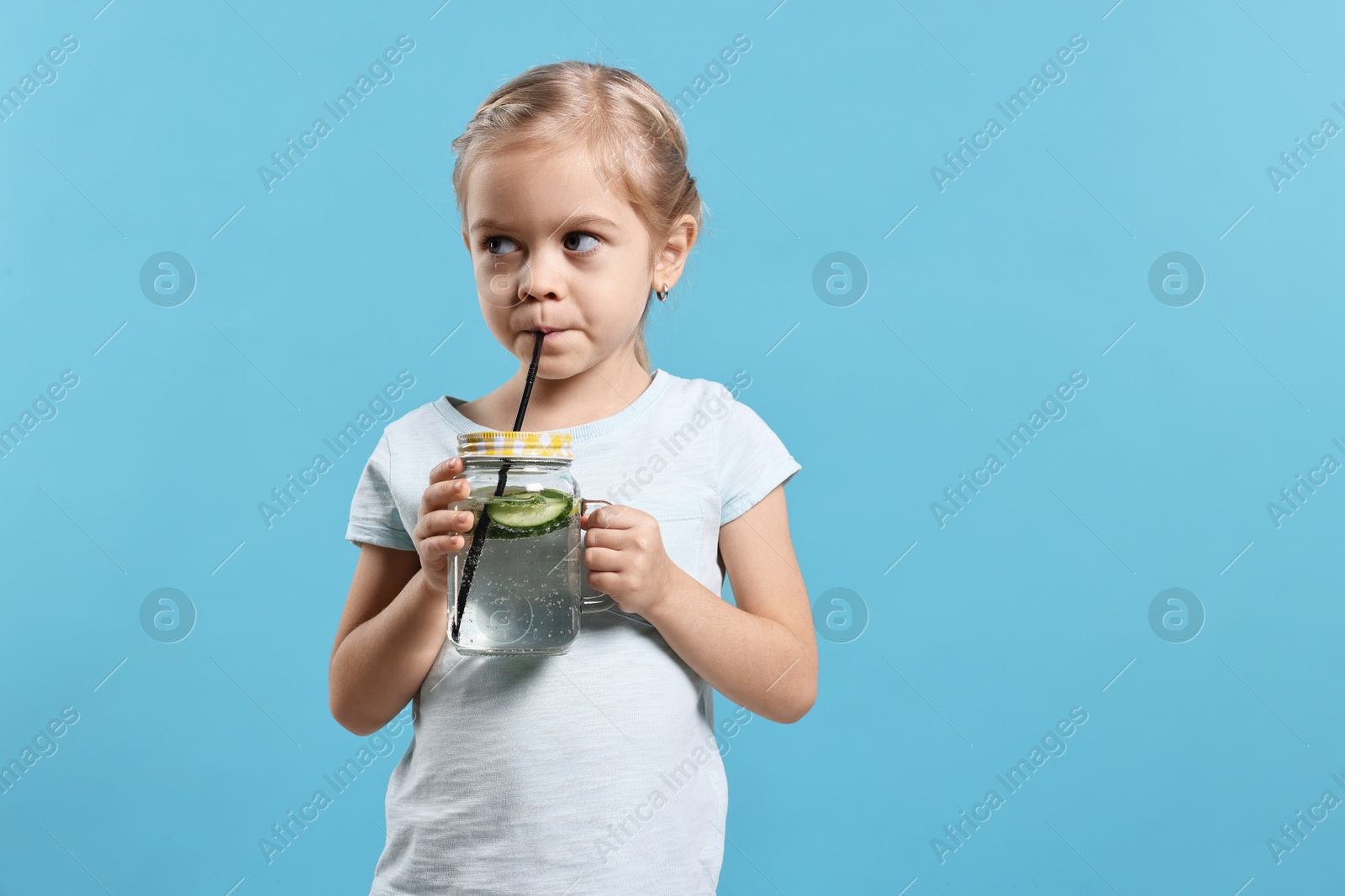 Photo of Girl drinking tasty cucumber water on light blue background, space for text. Refreshing drink