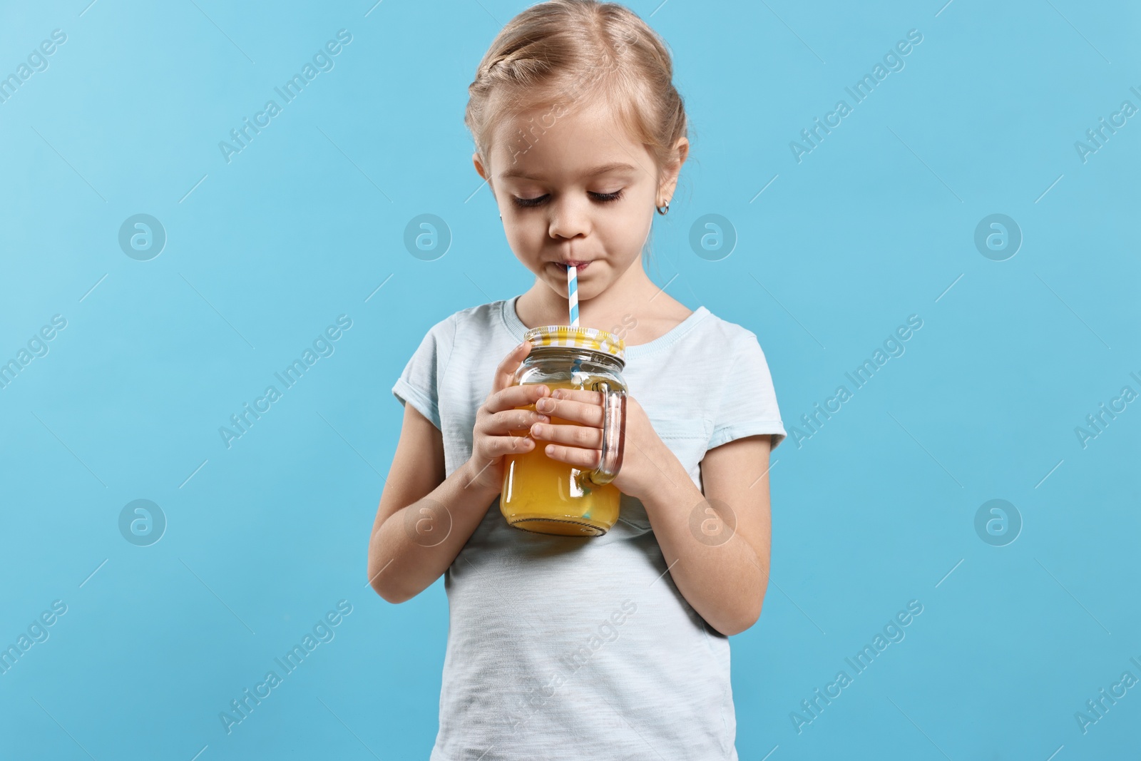 Photo of Girl drinking tasty orange juice on light blue background. Refreshing drink