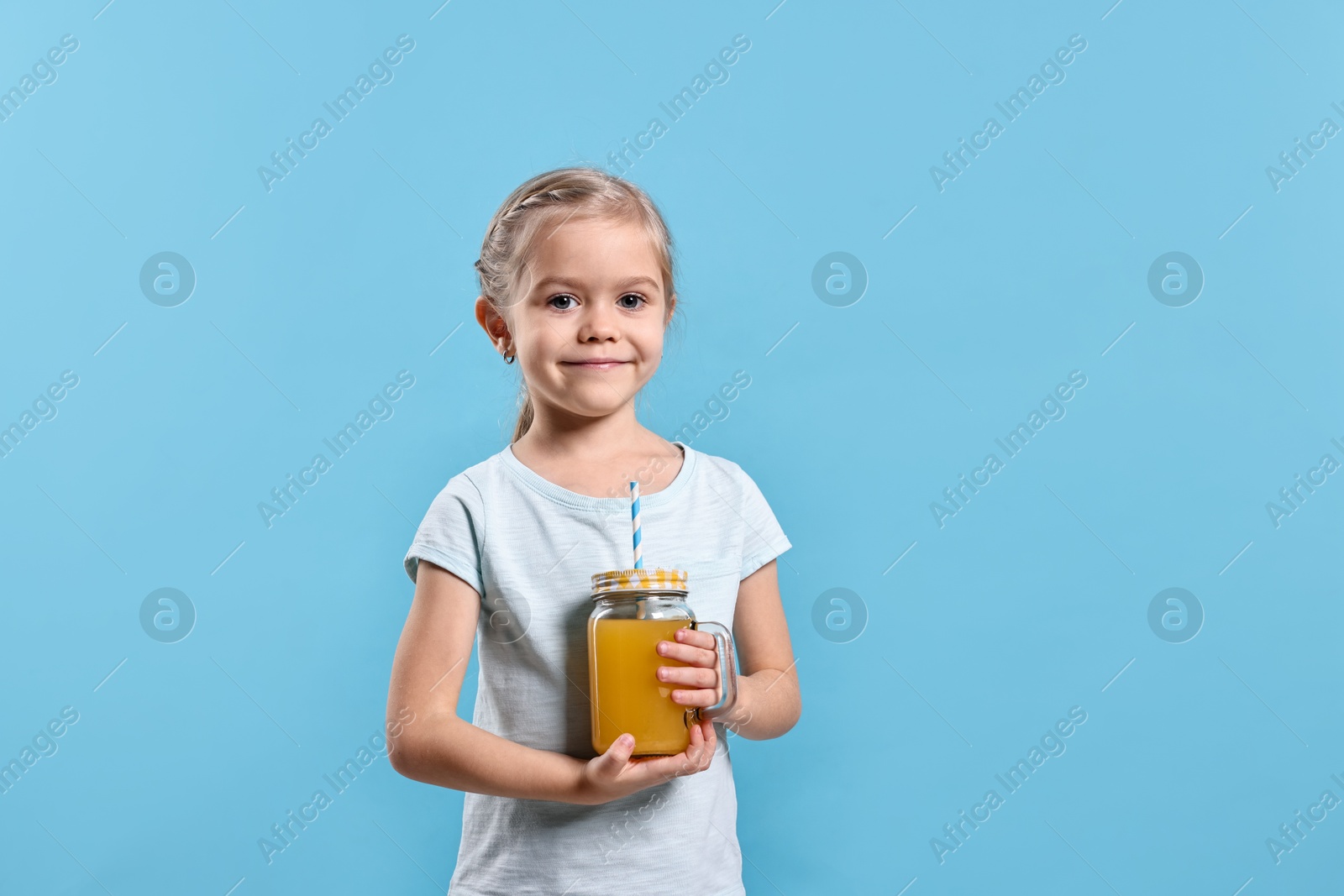 Photo of Girl with mason jar of orange juice on light blue background, space for text. Refreshing drink