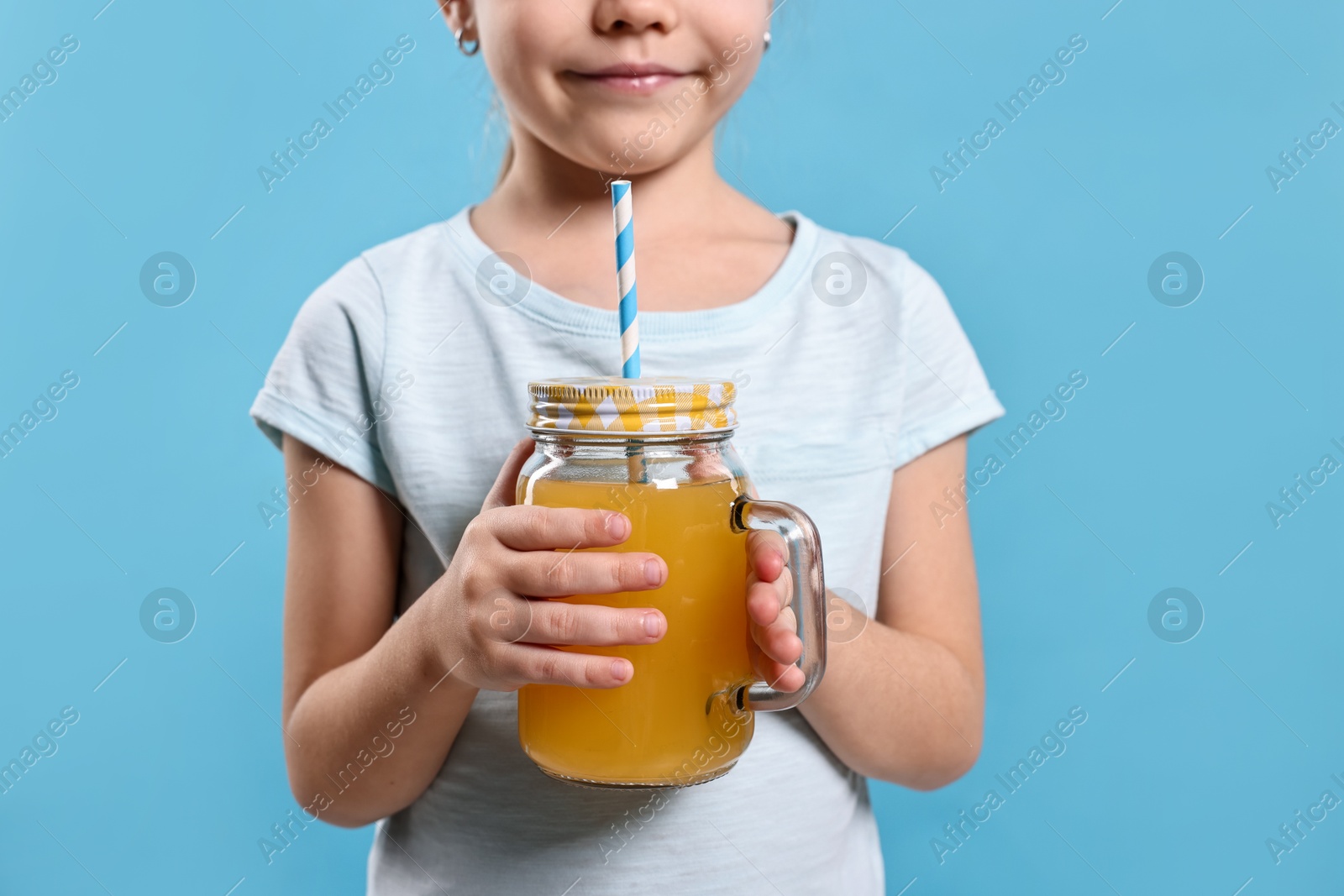 Photo of Girl with glass of orange juice on light blue background, closeup. Refreshing drink