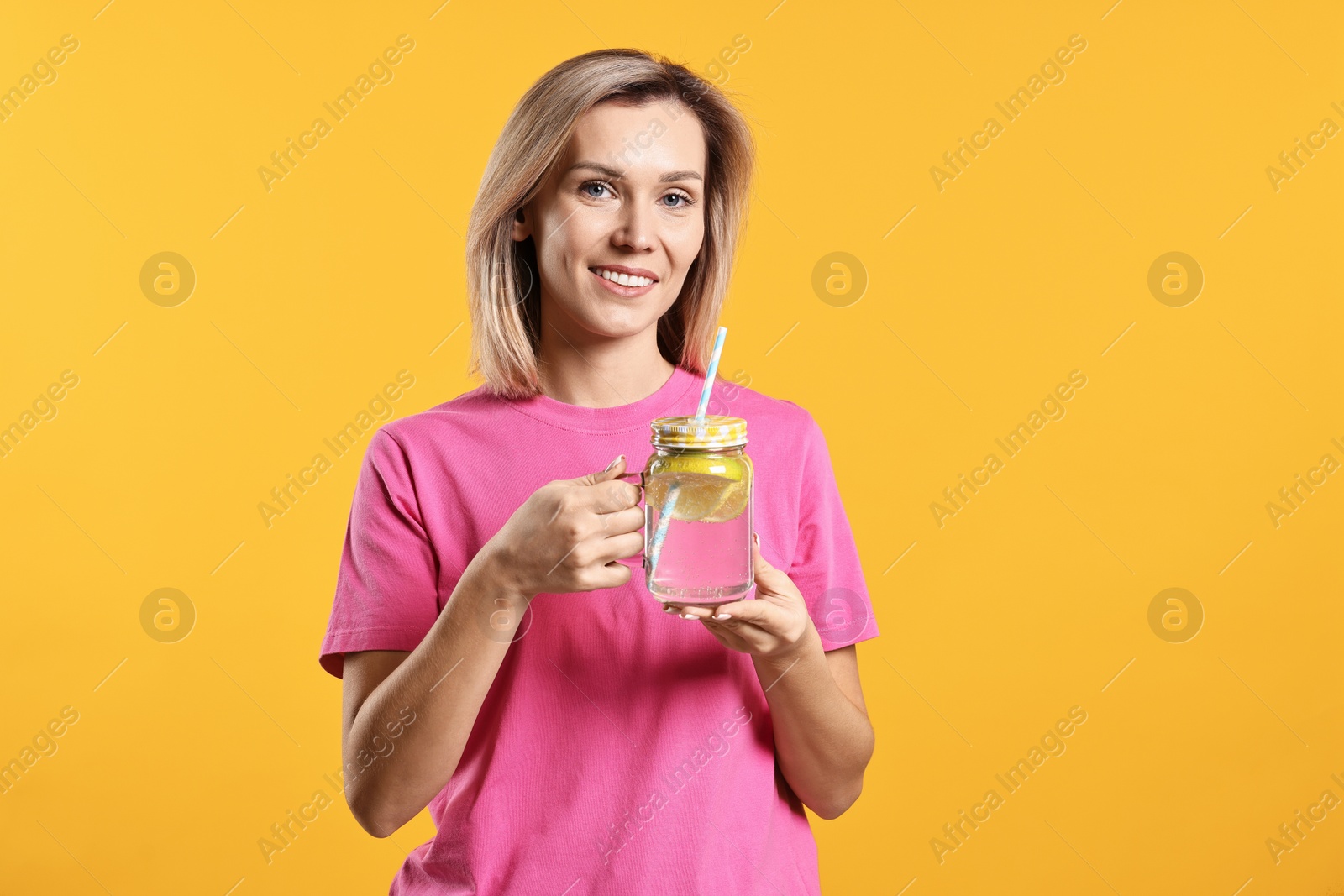 Photo of Woman with mason jar of lemonade on orange background. Refreshing drink