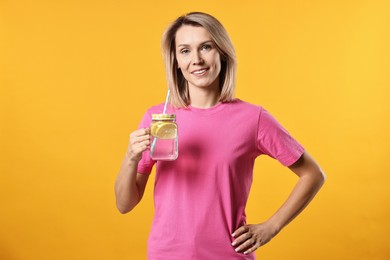 Photo of Woman with mason jar of lemonade on orange background. Refreshing drink