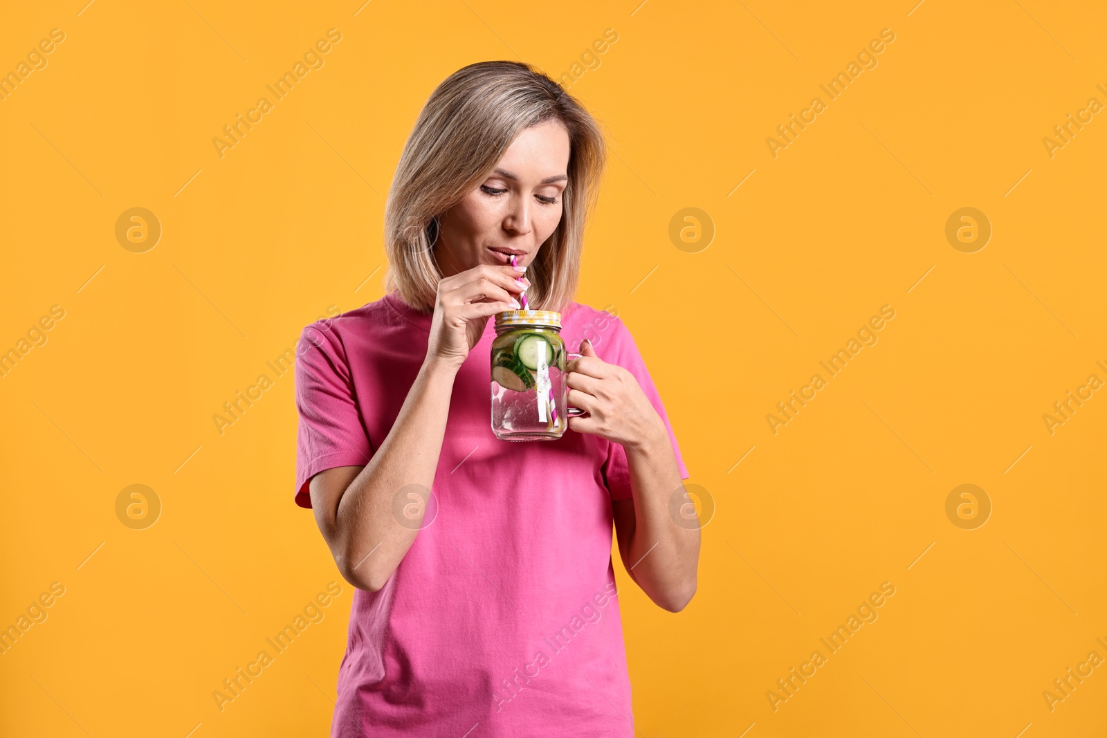 Photo of Woman drinking tasty cucumber water on orange background, space for text. Refreshing drink