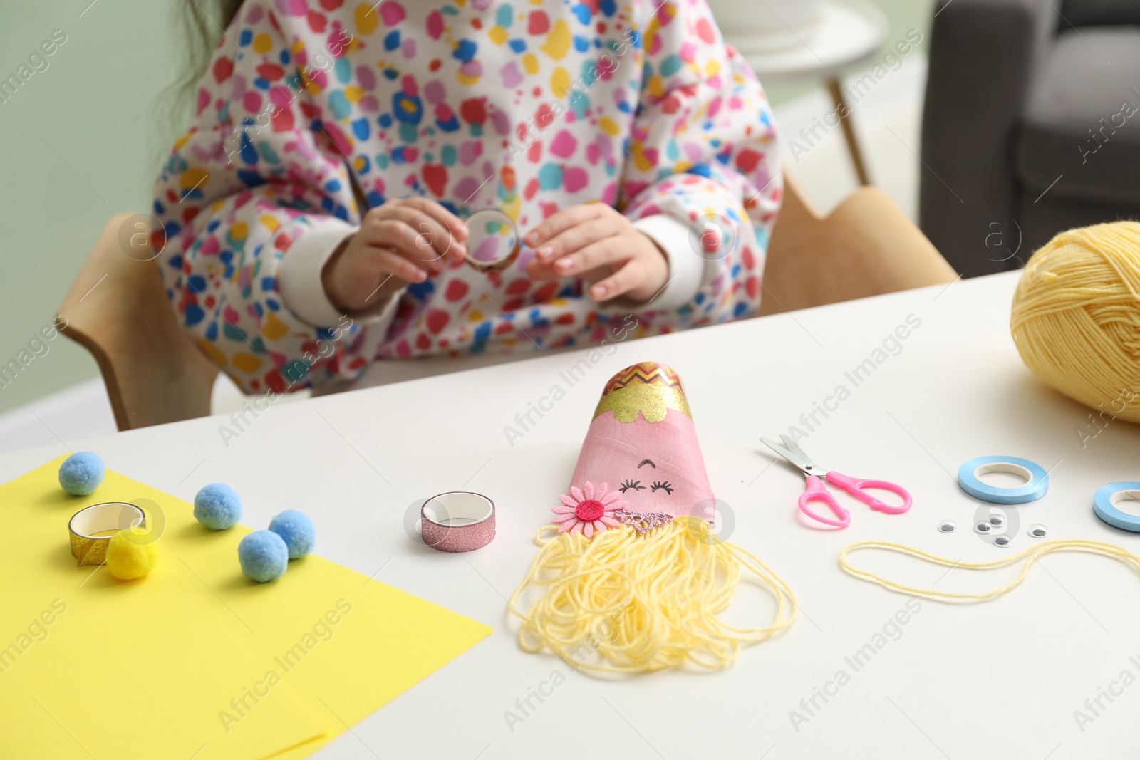 Photo of Little girl making craft at white table indoors, closeup. Child creativity