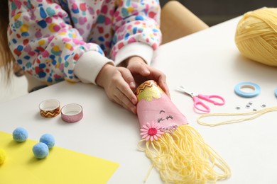 Photo of Little girl with handmade toy at white table, closeup. Child creativity and craft