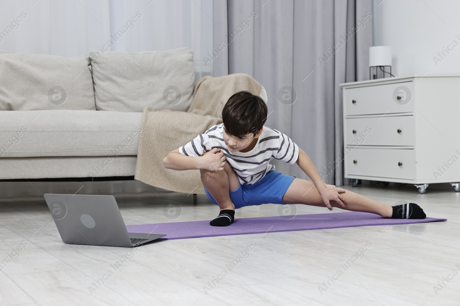 Photo of Little boy exercising near laptop at home. Morning routine