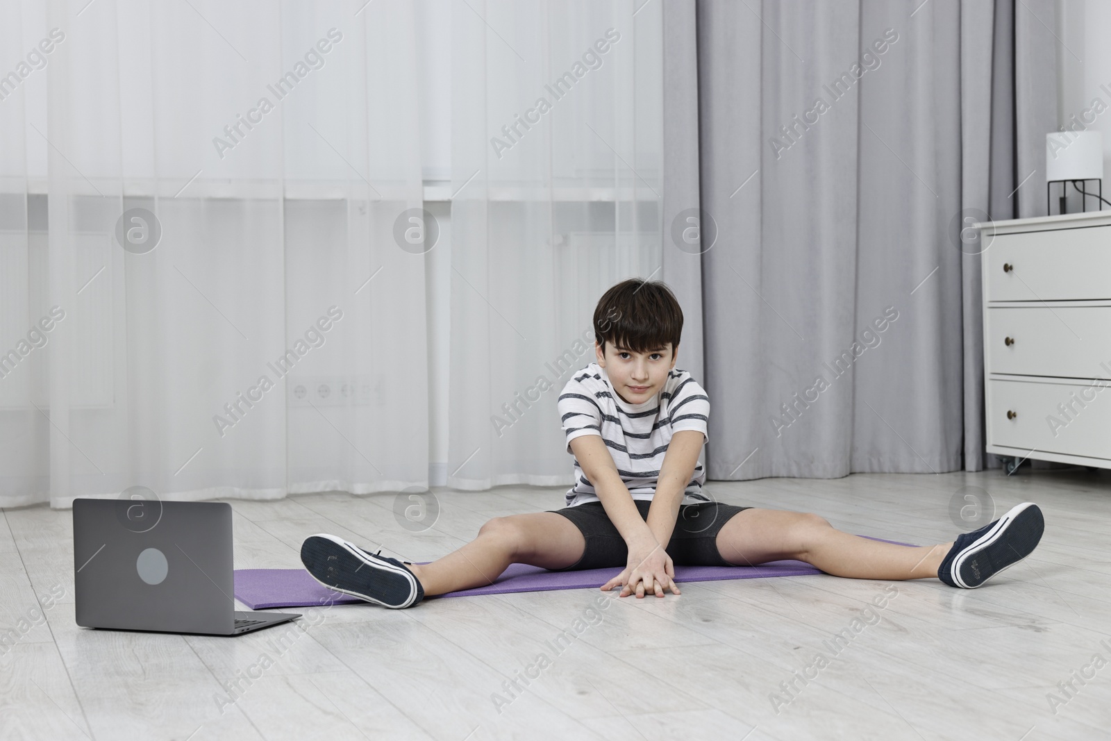 Photo of Little boy exercising near laptop at home. Morning routine