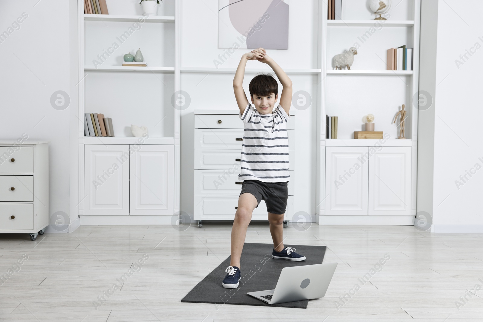 Photo of Little boy exercising near laptop at home. Morning routine