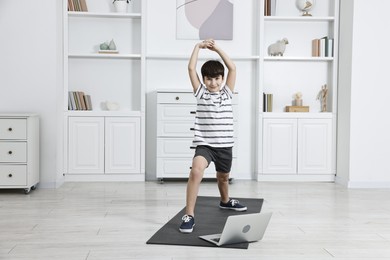 Photo of Little boy exercising near laptop at home. Morning routine