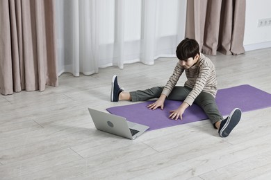 Photo of Little boy exercising near laptop at home. Morning routine